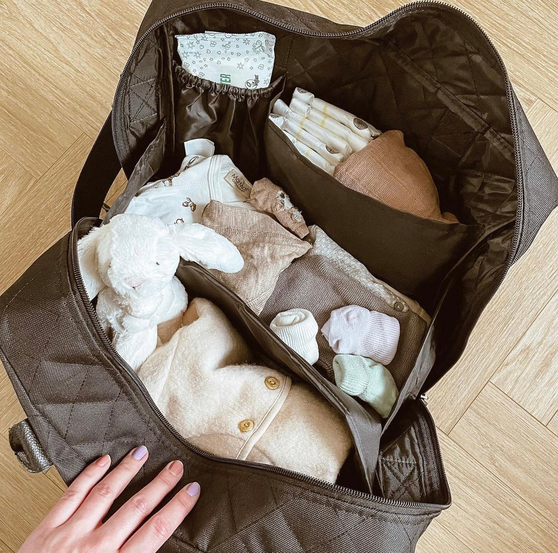 Stor og rummelig pusletaske i sort quilt set ovenfra med mange rum fyldt med bleer og babyudstyr